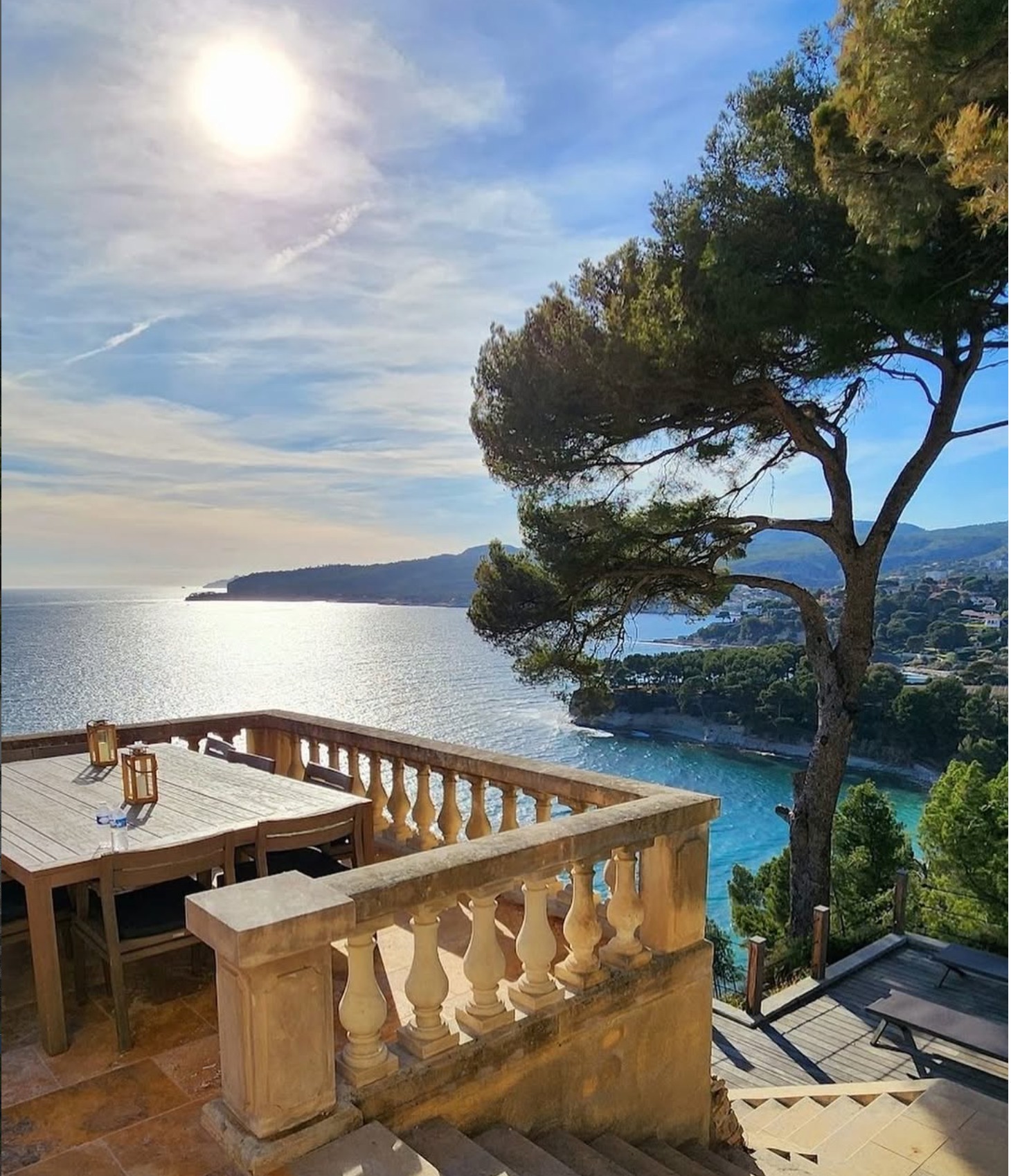Sunlit terrace with a stone balustrade and umbrella pine overlooking a turquoise Mediterranean cove near Cassis